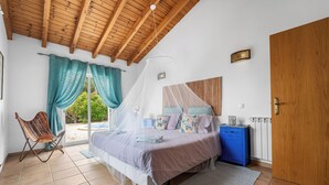 Ein Schlafzimmer mit Bett, Stuhl, Nachttisch, Kleiderschrank und einem Fenster mit Vorhängen.