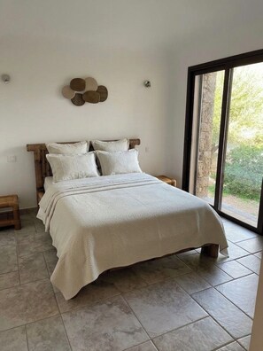 Ein Schlafzimmer mit einem Bett, einem hölzernen Kopfteil, einem großen Fenster und Blick ins Grüne.