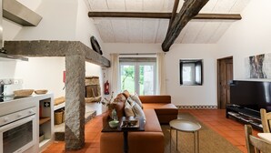 Een woonkamer met een stenen pilaar, een bank, een televisietoestel en een keuken met een fornuis.
