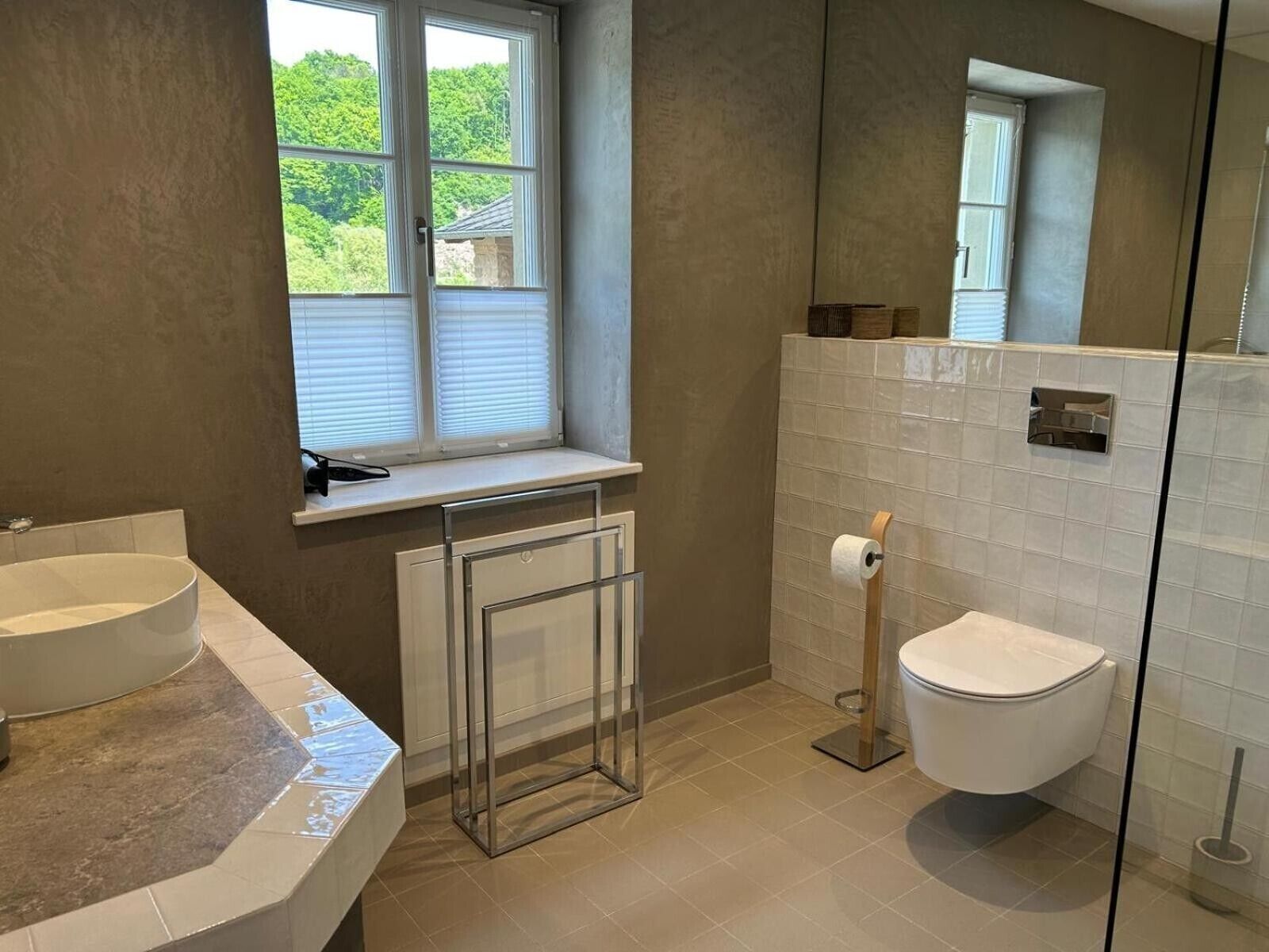 A bathroom with a window, a sink, a toilet, and a mirror.
