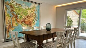 A dining area with a large map, a wooden table, and white chairs.