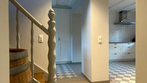 A staircase with a wooden barrel, a white door, and a kitchen with white cabinets and checkered flooring.