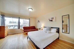 A bedroom with a bed, a wooden dresser, a red sofa, a window with curtains, and a wall-mounted mirror. - Walk to Othello Park & Light Rail: Quiet Escape (Seattle)