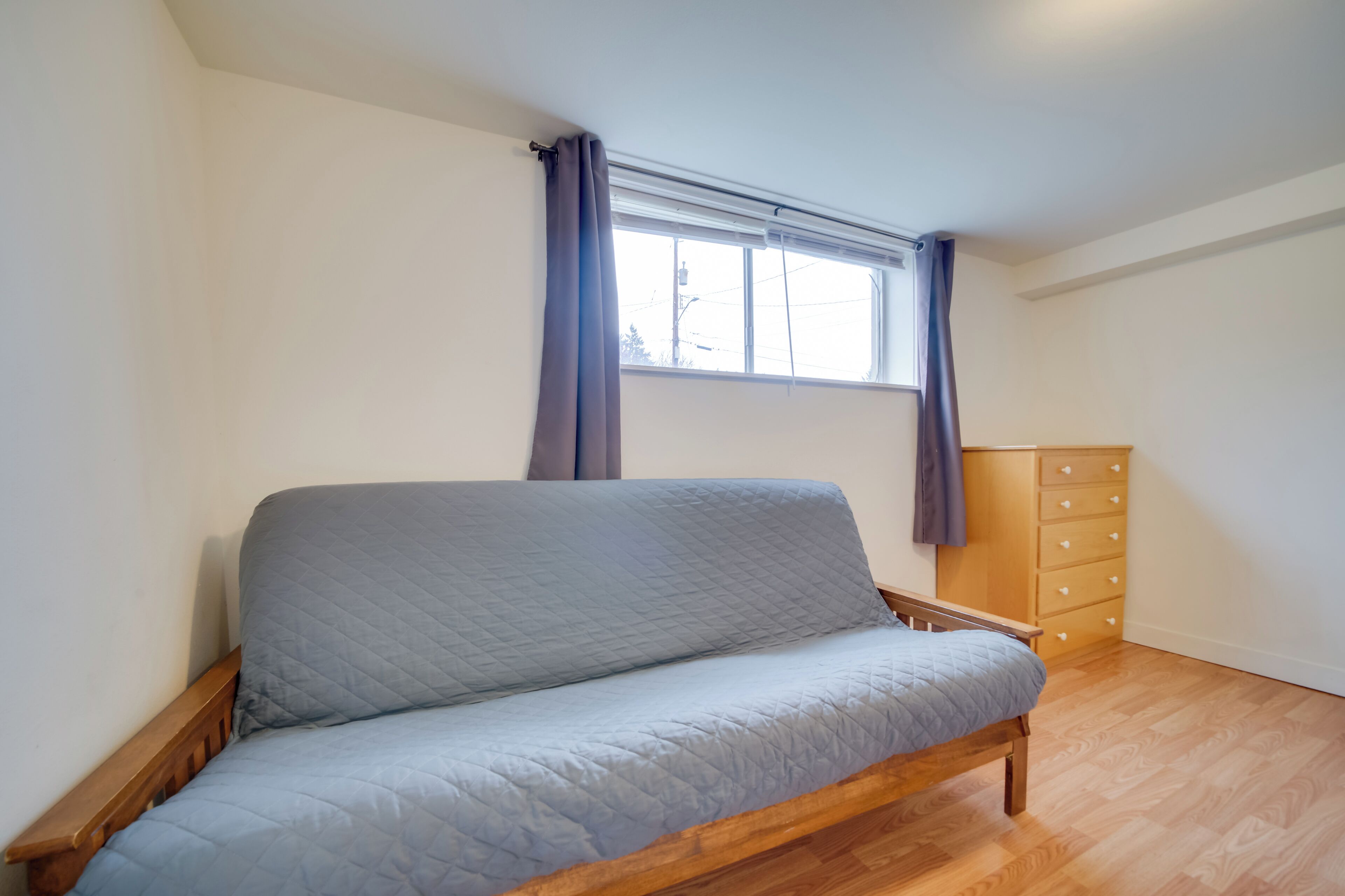 A room with a wooden bed, a window with curtains, and a wooden dresser.