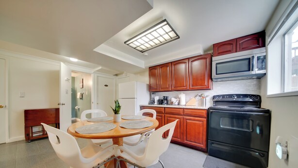 Une cuisine moderne avec des meubles en bois, un cuisinière noire, un four à micro-ondes et un coin repas comprenant une table ronde et des chaises blanches.