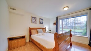 Une chambre à coucher avec un lit en bois, une table de chevet, une petite armoire et une fenêtre donnant sur l’extérieur.