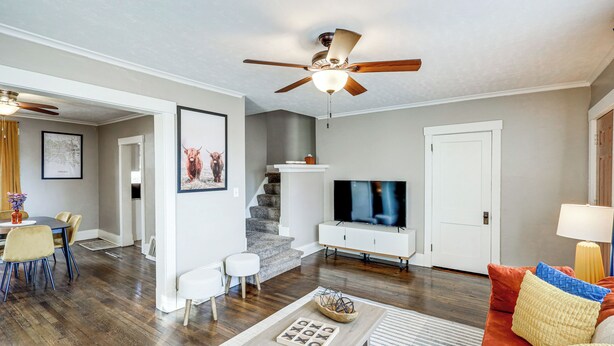 A spacious living room with a wooden floor, a ceiling fan, a TV, a sofa, and a dining area with chairs and a table. - 3 Mi to Dtwn: Omaha Escape w/ Game Room & Patio! (Omaha)