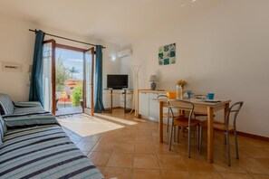 A room with a sofa, a dining table with chairs, a TV, and a window with curtains. - GuestHost - Cozy 50 square meters villa, perfect for four people, with direct access from the garden.The property is just a 12-minute drive from Porto Giunco ​​beach and a 15-minute drive from Capo Carbonara beach.The accommodation comprises a living (Villasimius)