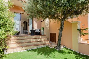 A building with a staircase leading to a covered porch, a tree, and a small garden area. - GuestHost - Cozy 50 square meters villa, perfect for four people, with direct access from the garden.The property is just a 12-minute drive from Porto Giunco ​​beach and a 15-minute drive from Capo Carbonara beach.The accommodation comprises a living (Villasimius)