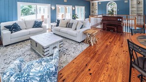 Ein großzügiges Wohnzimmer mit Holzboden, einem Klavier und einer Treppe, die in eine obere Ebene führt.