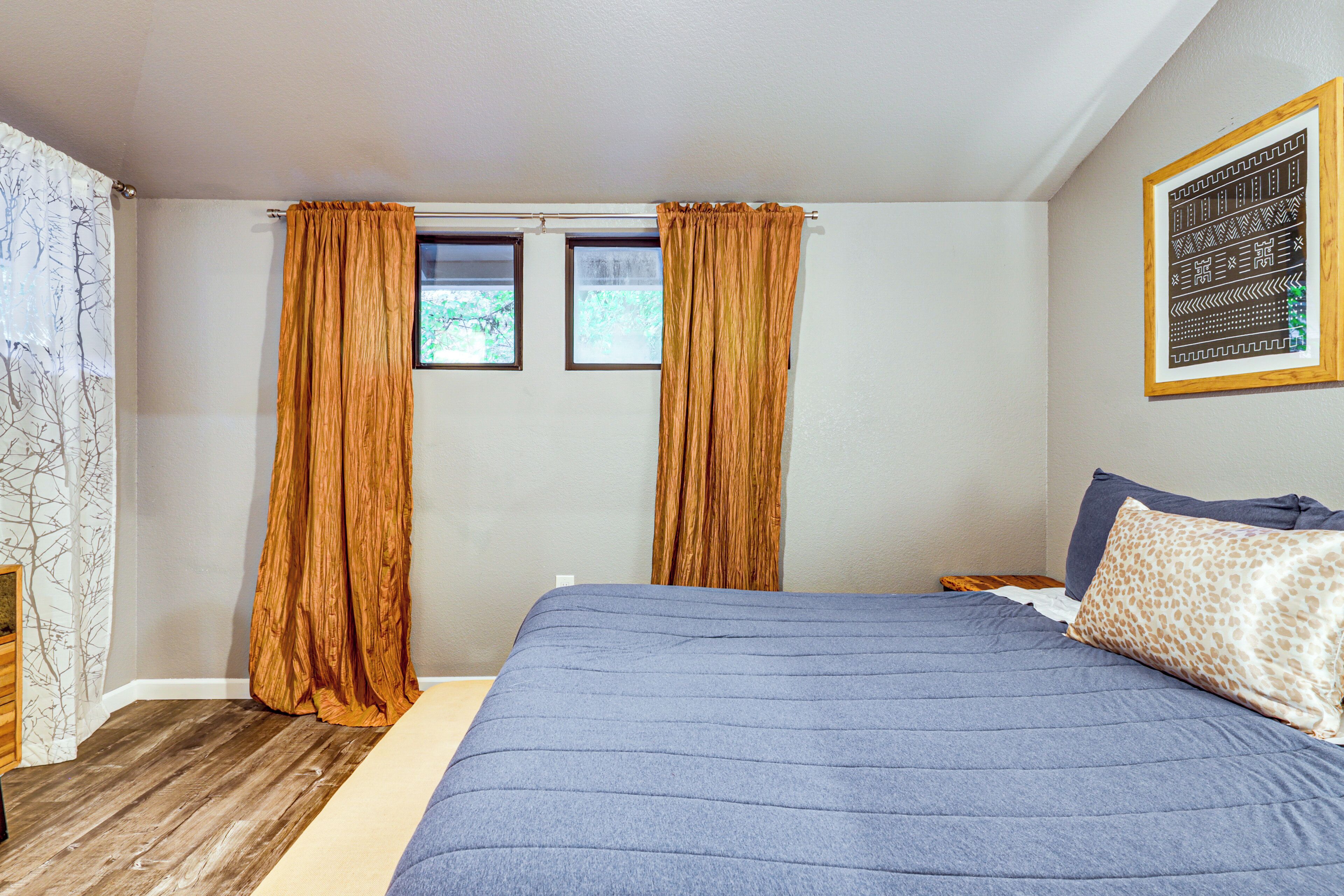 A bedroom with a large bed, two windows, and a framed artwork on the wall.