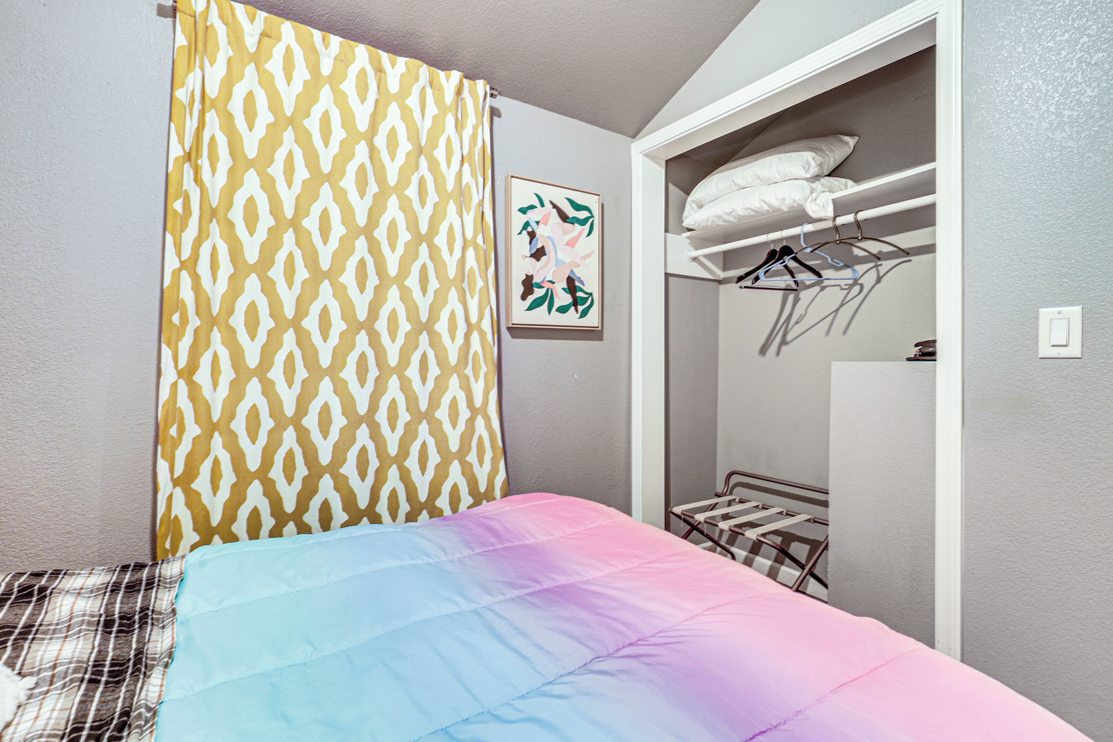 A bedroom with a bed, a patterned curtain, a wall-mounted picture, a built-in wardrobe, and a hanging rack.