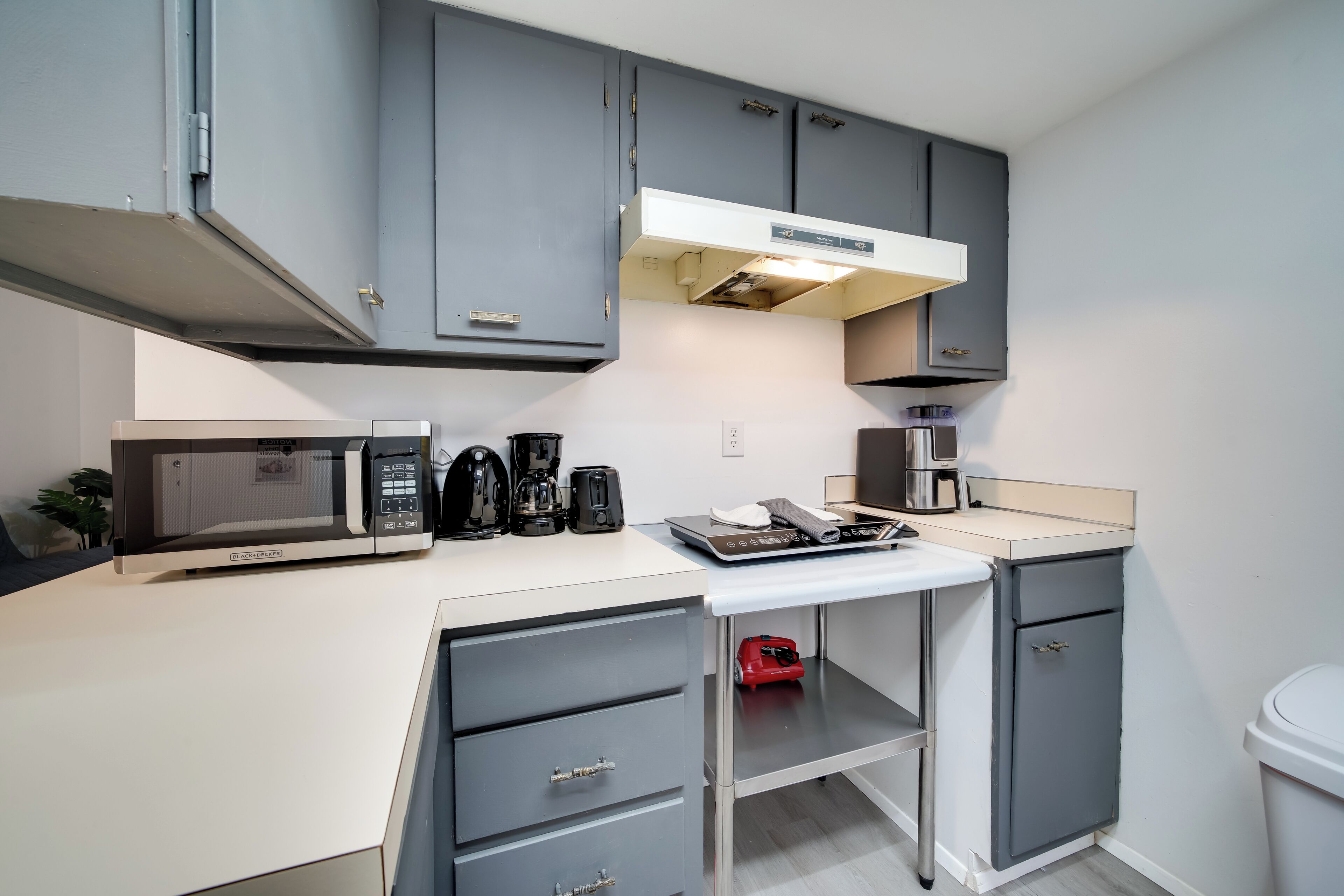 A compact kitchen with grey cabinets, a microwave, a coffee maker, and a toaster.