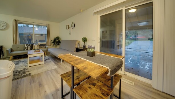 A modern living room with a sofa, a wooden coffee table, and a sliding glass door leading to a covered outdoor area. - Eastside Tech Hub Home Base Near I-90 & Factoria! (Bellevue)