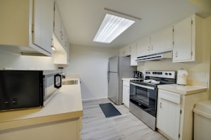 A modern kitchen with white cabinets, a stainless steel refrigerator, a microwave, an oven, and a gas stove.