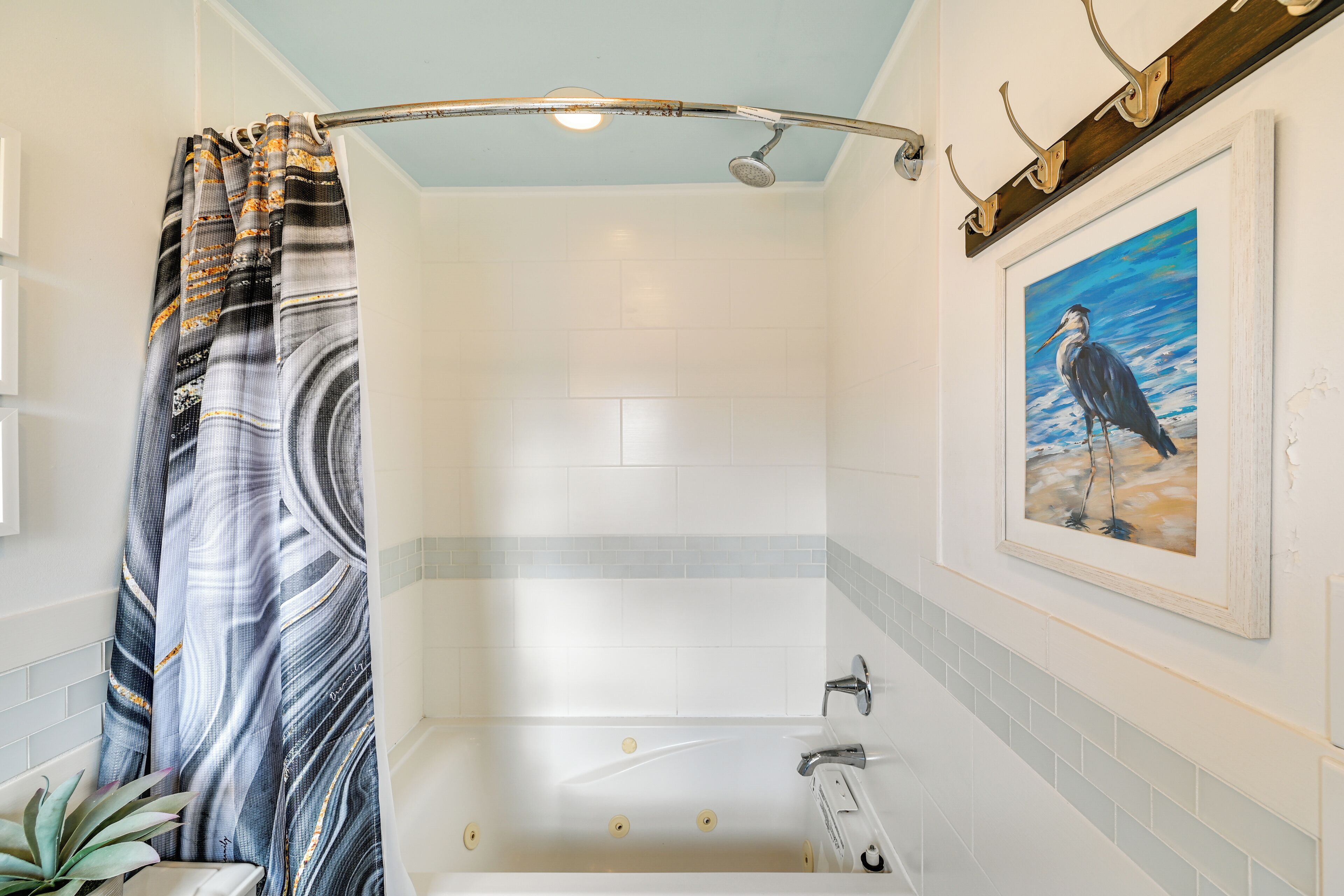 A bathroom with a bathtub, a shower curtain, a potted plant, and a framed painting on the wall.