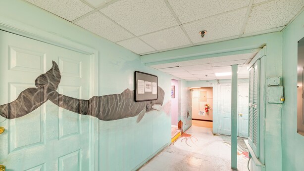 A hallway with teal walls, a door with a large, abstract sculpture, and a framed notice on the wall. - Prime Walkable Location! Ocean City Studio (Ocean City)