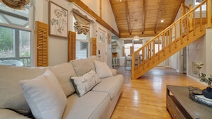 A spacious living room with a wooden staircase, a sofa, and a dining area. - 5 Forested Acres! Peaceful Retreat 4 Mi to Helen (Sautee Nacoochee)