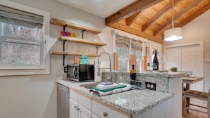 A kitchen with granite countertops, a built-in dishwasher, wooden beams, and a window with a view of trees. - 5 Forested Acres! Peaceful Retreat 4 Mi to Helen (Sautee Nacoochee)