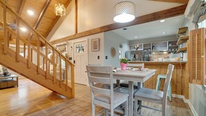 A spacious kitchen with wooden beams, a dining area with white chairs, and a staircase leading to another level. - 5 Forested Acres! Peaceful Retreat 4 Mi to Helen (Sautee Nacoochee)