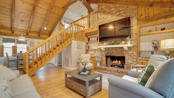 A spacious living room with a wooden staircase, a fireplace, and a television mounted above it. - 5 Forested Acres! Peaceful Retreat 4 Mi to Helen (Sautee Nacoochee)
