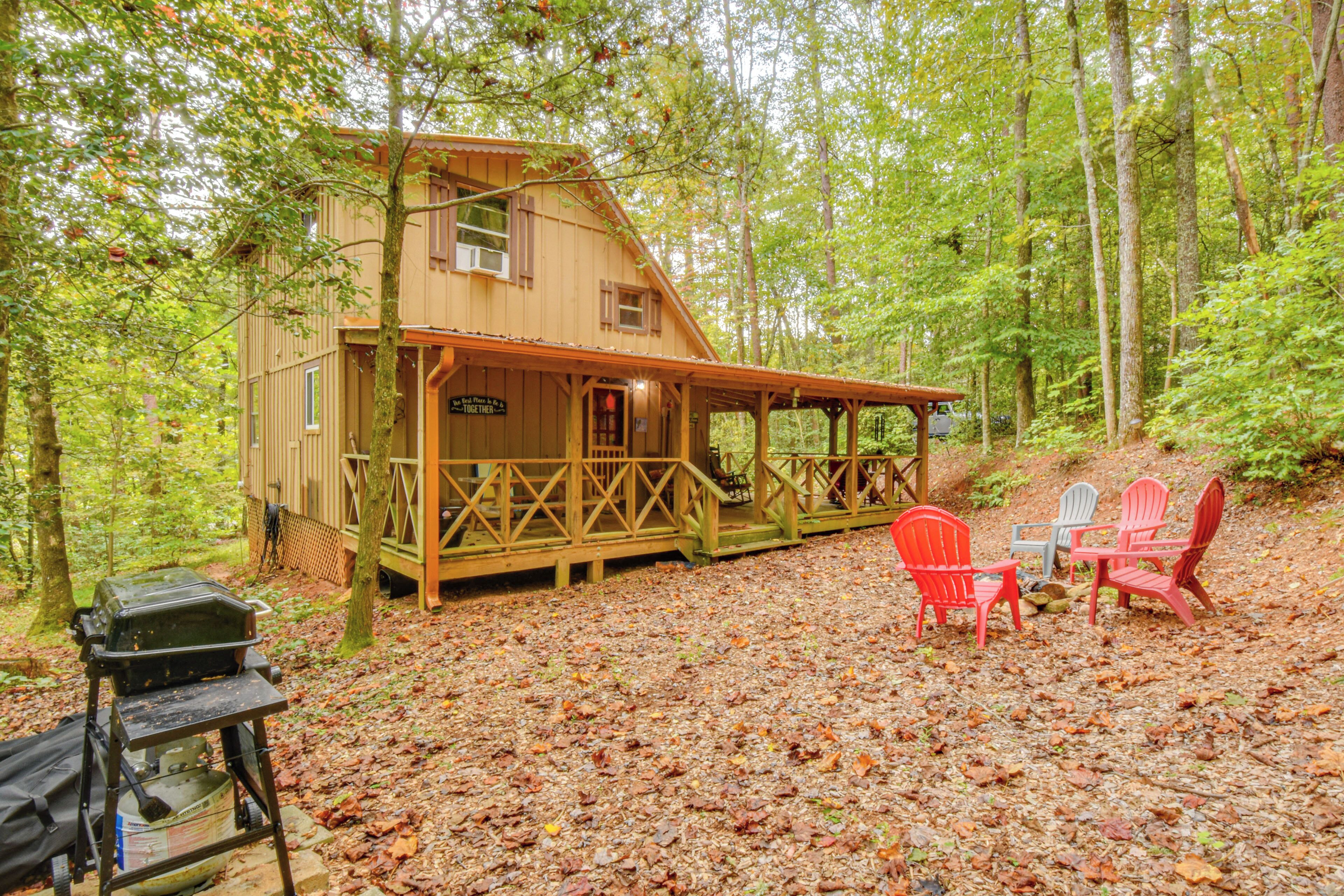 Une cabane avec une véranda, des fauteuils Adirondack rouges et gris, et un barbecue.