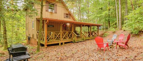 Une cabane avec une véranda, des fauteuils Adirondack rouges et gris, et un barbecue.