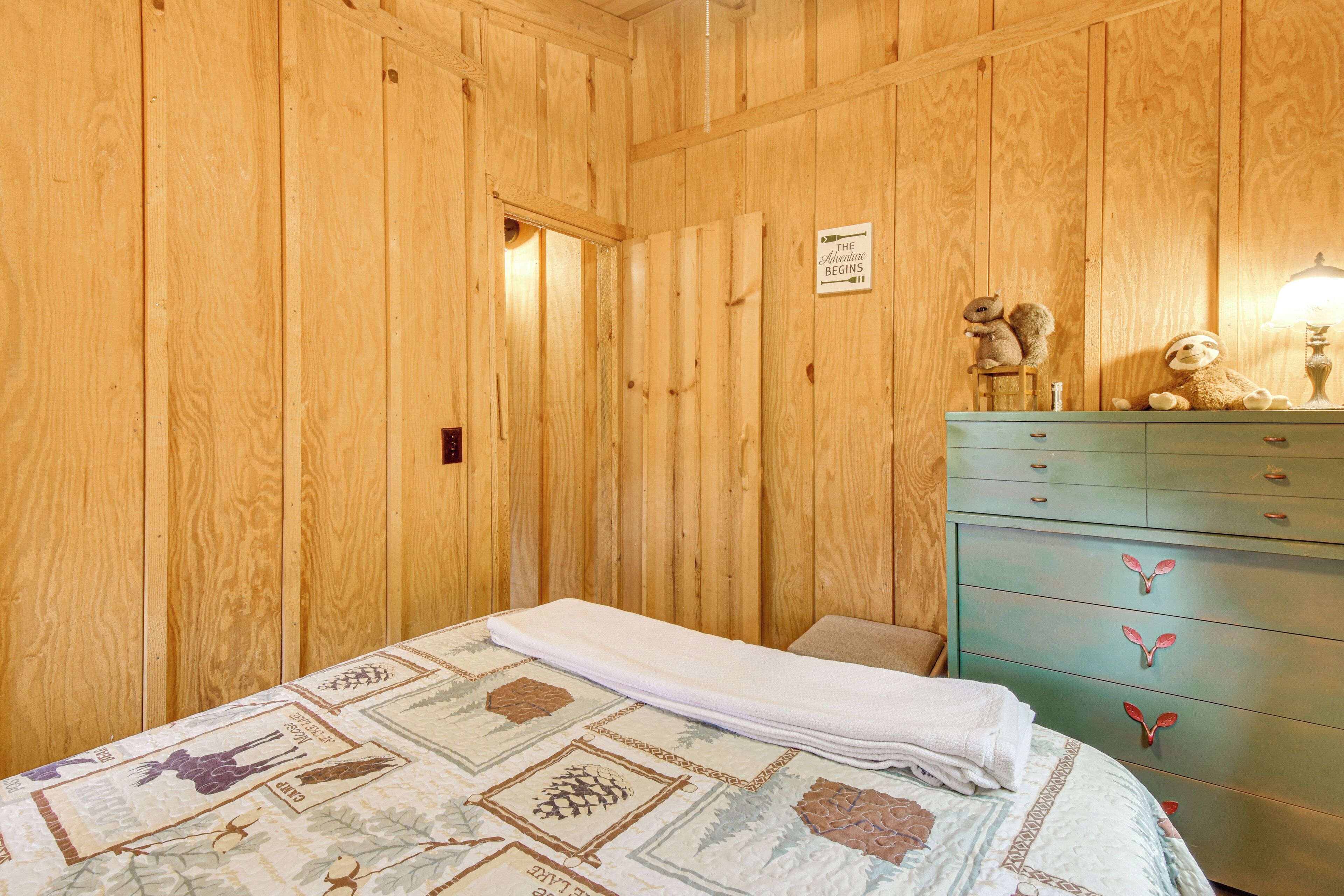 A wooden-paneled room with a bed, a dresser, and a sign on the wall.