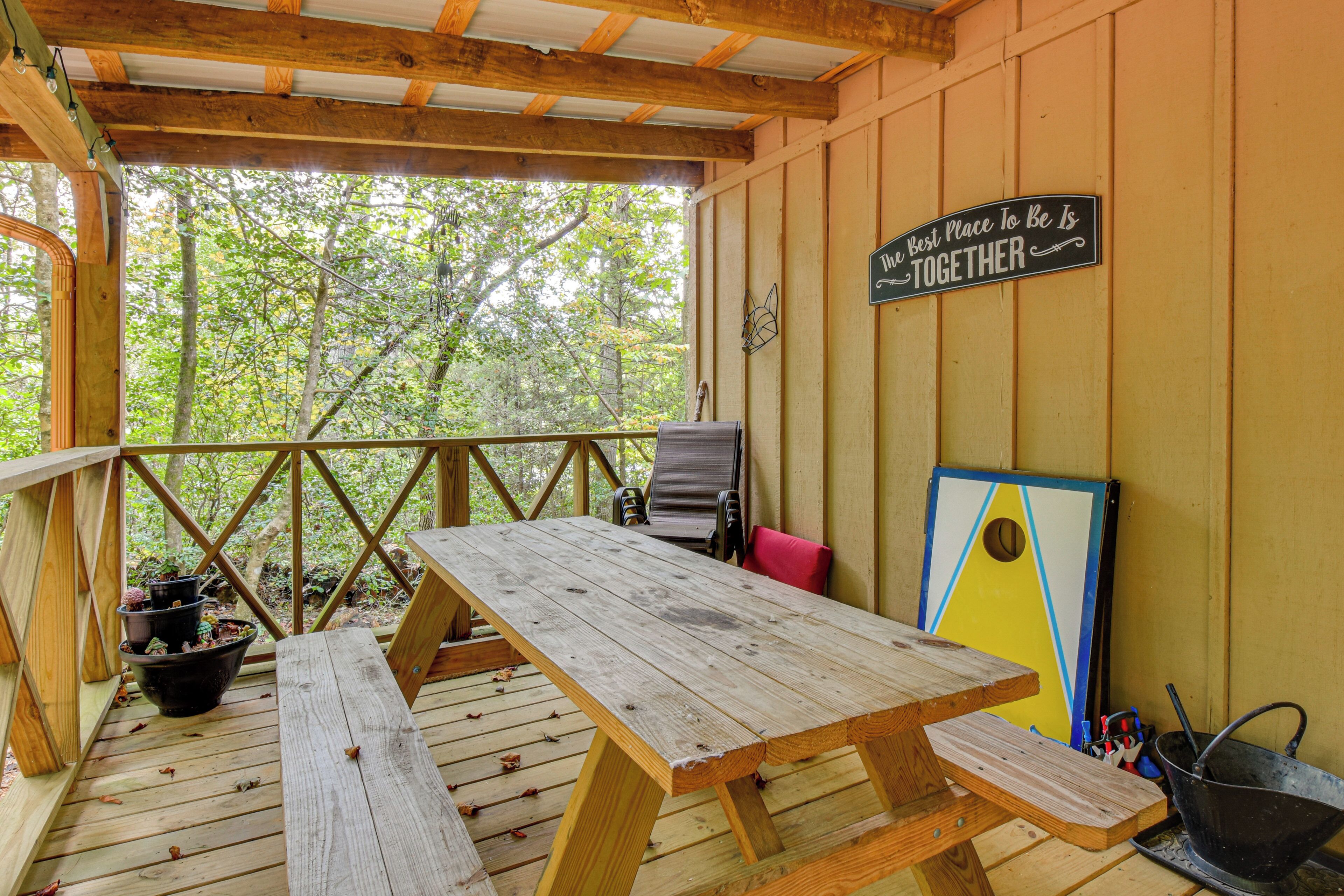 Une terrasse en bois avec une table de pique-nique et des chaises, entourée d’arbres.