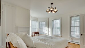 Una camera da letto con un letto grande, un comodino in legno, un lampadario e diverse finestre.
