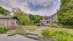 Una proprietà residenziale con patio lastricato, un piccolo angolo relax all'aperto, recinzione in legno e giardino con diverse piante.
