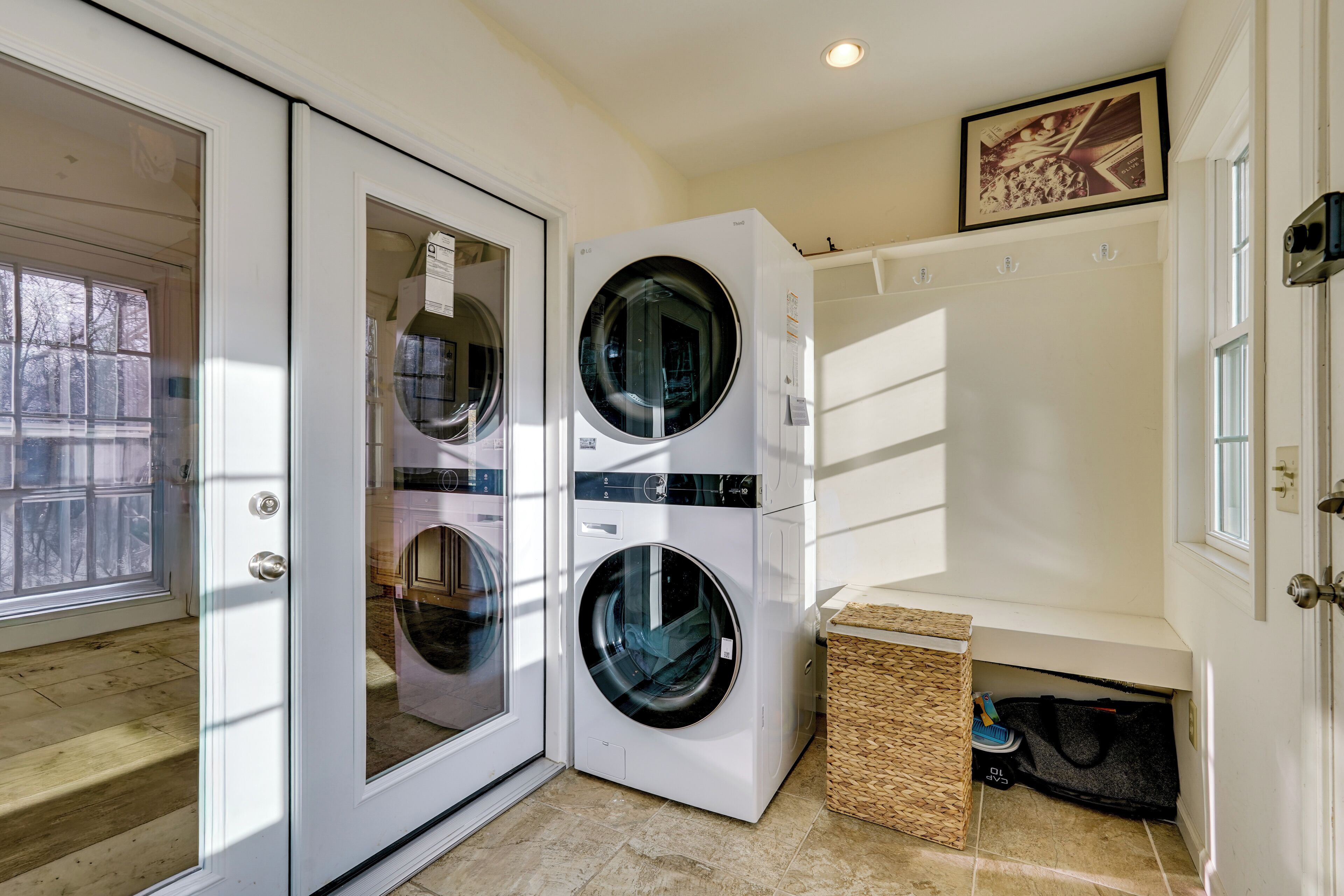 A laundry room with two front-loading washing machines, a wicker basket, and a small trash bin.