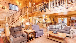 Ein geräumiges Blockhaus-Interieur mit einer Holztreppe, einem Essbereich und einem Wohnzimmer, möbliert mit Sofas und einem Couchtisch.