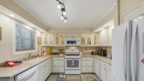 Une cuisine avec des meubles blancs, un four à micro-ondes, une cuisinière et un réfrigérateur.