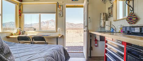 A bedroom with a large bed, a desk, and a view of the desert through an open door.