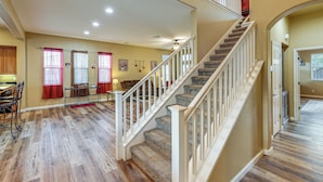 A spacious living area with hardwood flooring, a staircase with white railings, and a dining area with a table and chairs. - Napa Nearby! Large Home w/ Hot Tub & Dtwn Access (Suisun City)