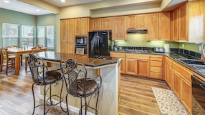 A kitchen with wooden cabinets, a black refrigerator, a stove, and two bar stools. - Napa Nearby! Large Home w/ Hot Tub & Dtwn Access (Suisun City)