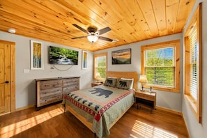 Ein Schlafzimmer mit Holzboden, einem Bett mit Bärenmotiv, einem Deckenventilator und großen Fenstern mit Jalousien.