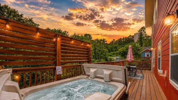 Un jacuzzi en una terraza de madera con vista al atardecer, una valla de madera y un pequeño edificio con un paraguas.