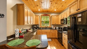 Cocina con armarios de madera, encimeras de granito, refrigerador de acero inoxidable y ventana con vista a zonas verdes.