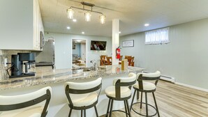A modern kitchen with granite countertops, a built-in oven, and a coffee maker. There are four bar stools with cushioned seats. The kitchen has a large island with a sink and a window with white curtains. - 3 Acres of Serenity! Countryside Home in Dickinson (Dickinson)
