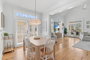 A spacious dining area with a wooden table and white chairs, large windows with blinds, and a ceiling fan. - Idle Hour in WaterColor | 2bd + Loft, 2 bikes, Steps to WaterColor Beach Club (Santa Rosa Beach)