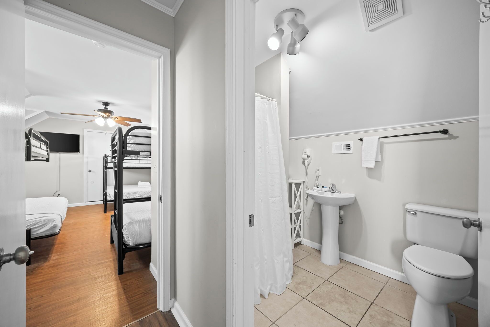 Una habitación con literas, baño con lavamanos e inodoro, y ventilador de techo.
