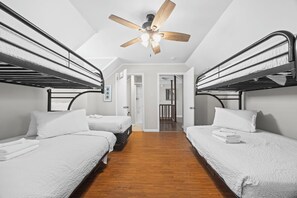 Une chambre avec des lits superposés, un ventilateur de plafond et un plancher en bois.