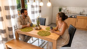 Una cocina moderna con una mesa de madera, dos sillas, un banco y un comedor con vistas a través de una ventana con cortinas.
