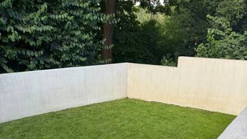 Zona de jardí rectangular amb superfície plana, envoltada per una paret baixa de formigó i un adorn de pedres a la part inferior.
