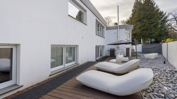 Une terrasse extérieure moderne avec des chaises longues blanches, une plateforme en bois et un bâtiment blanc doté de grandes fenêtres.