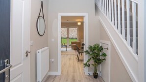 Um corredor com piso de madeira, um vaso de planta, um radiador branco e uma porta que dá para um quarto com uma cadeira e uma mesa.