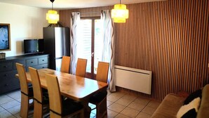 A dining area with a table and chairs, a television on a cabinet, and a radiator on the wall. - Chalet for 7 people - Les Flocons du Soleil (LE DEVOLUY)