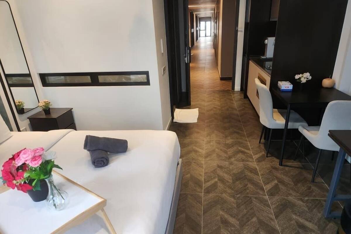 Habitación de hotel con cama, escritorio, silla, una mesita con un florero y un espejo.